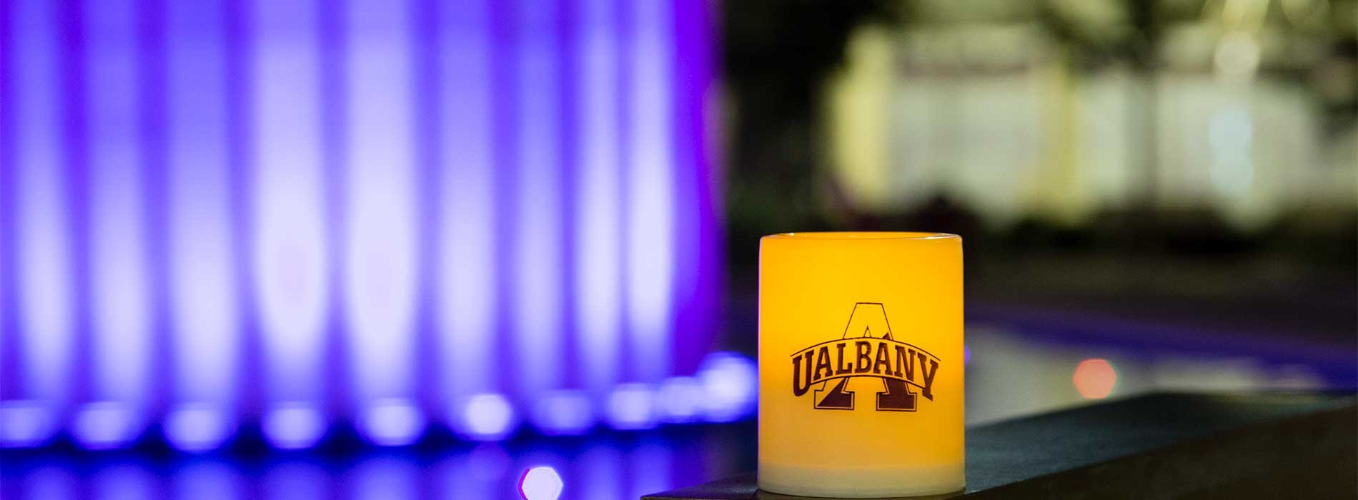 A UAlbany Candle sits near the main fountain and Carillon lit up in purple.