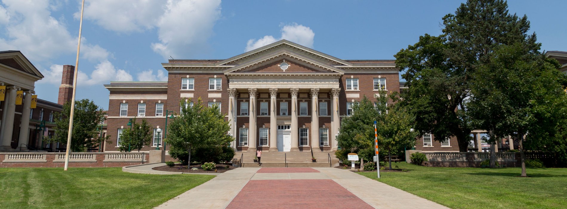 A brick Downtown Campus building with six tall columns and a brick walkway on a sunny day.
