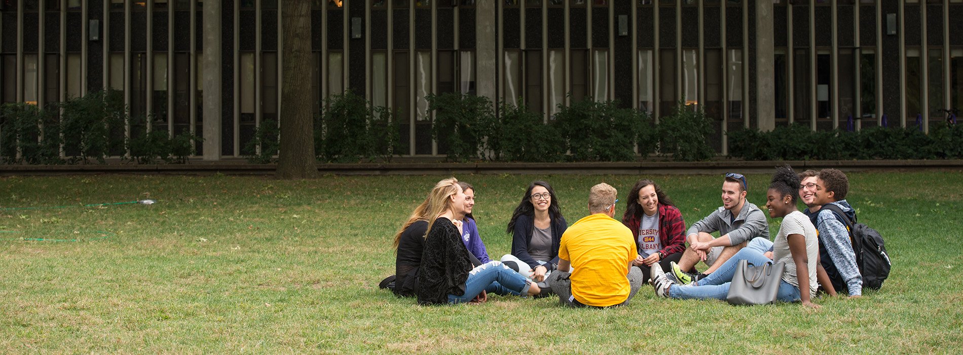 10 students sit in a circle on the grass outside a residence hall