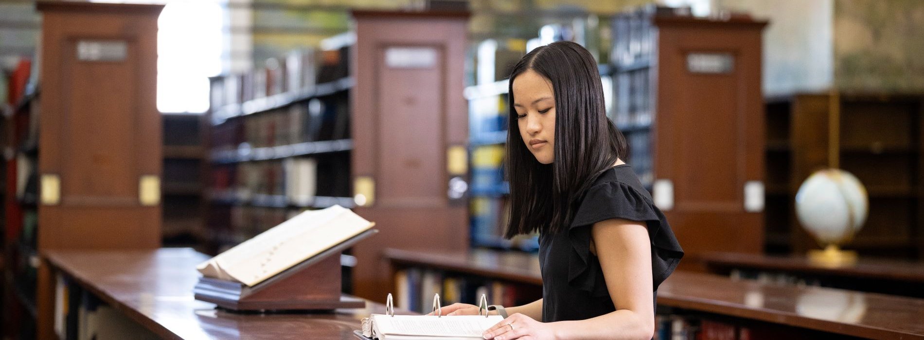 Female student in the UAlbany Downtown Library reading from a large ringed binder.