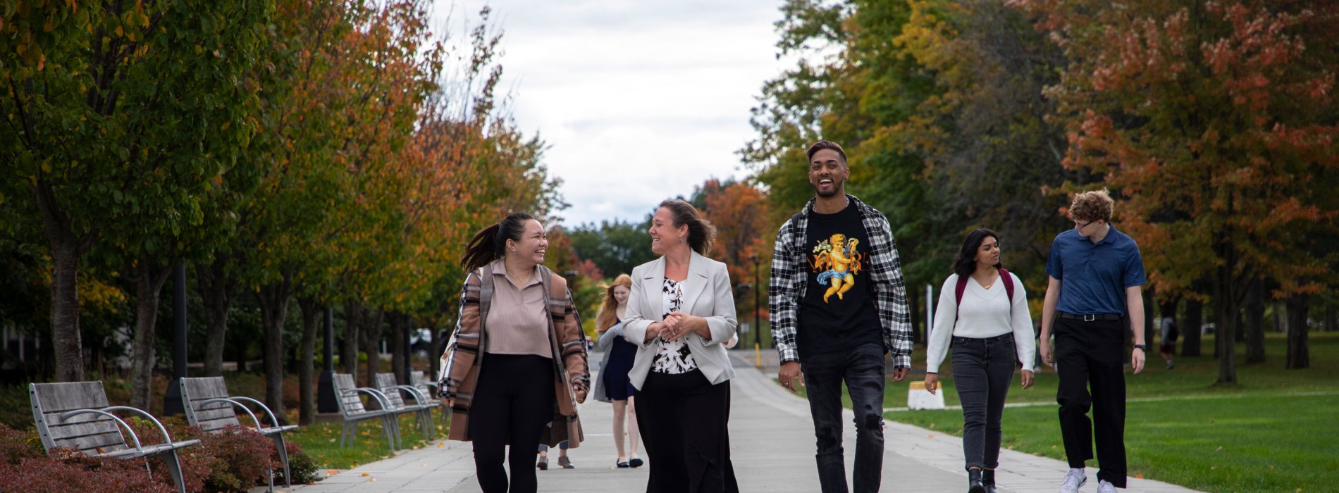 Vice Provost & Dean of Undergraduate Education JoAnne Malatesta smiles and gestures as she walks and talks with four students on UAlbany's campus on a cloudy fall day. 