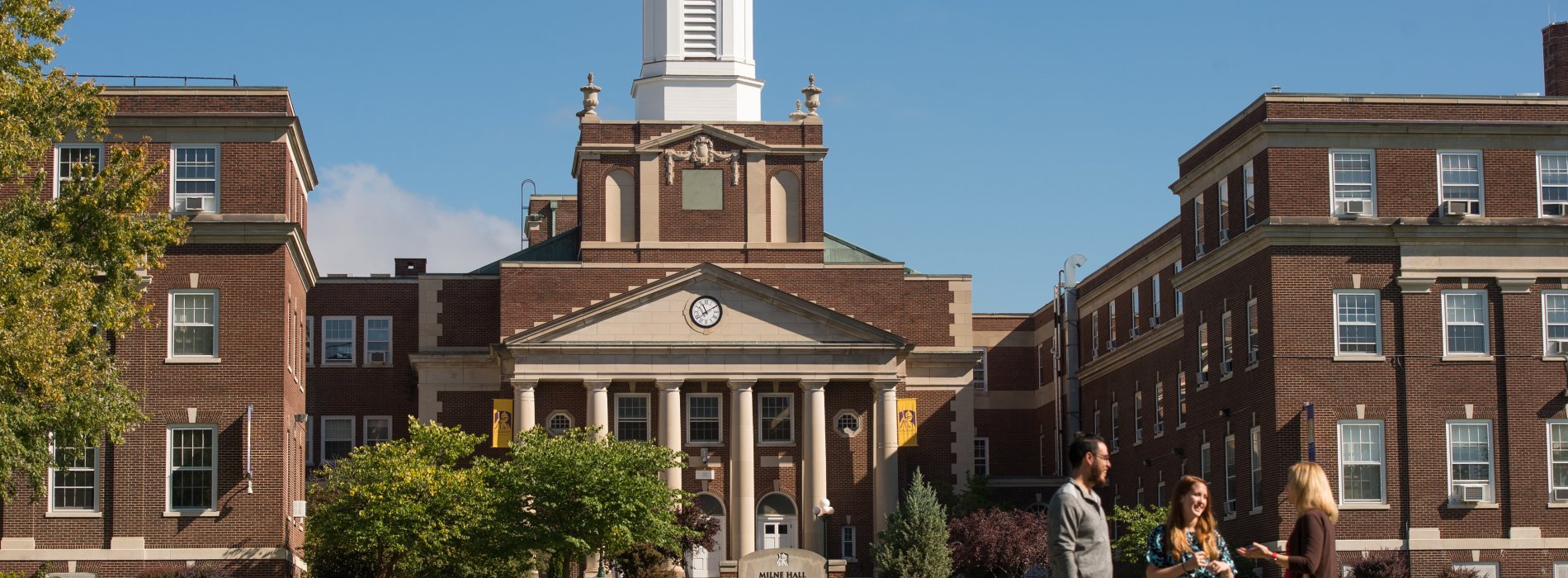 Three people having a conversation in front of the UAlbany Downtown campus.