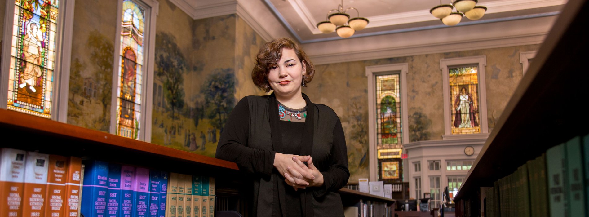 A woman in a black sweater stands inside an ornately decorated library.