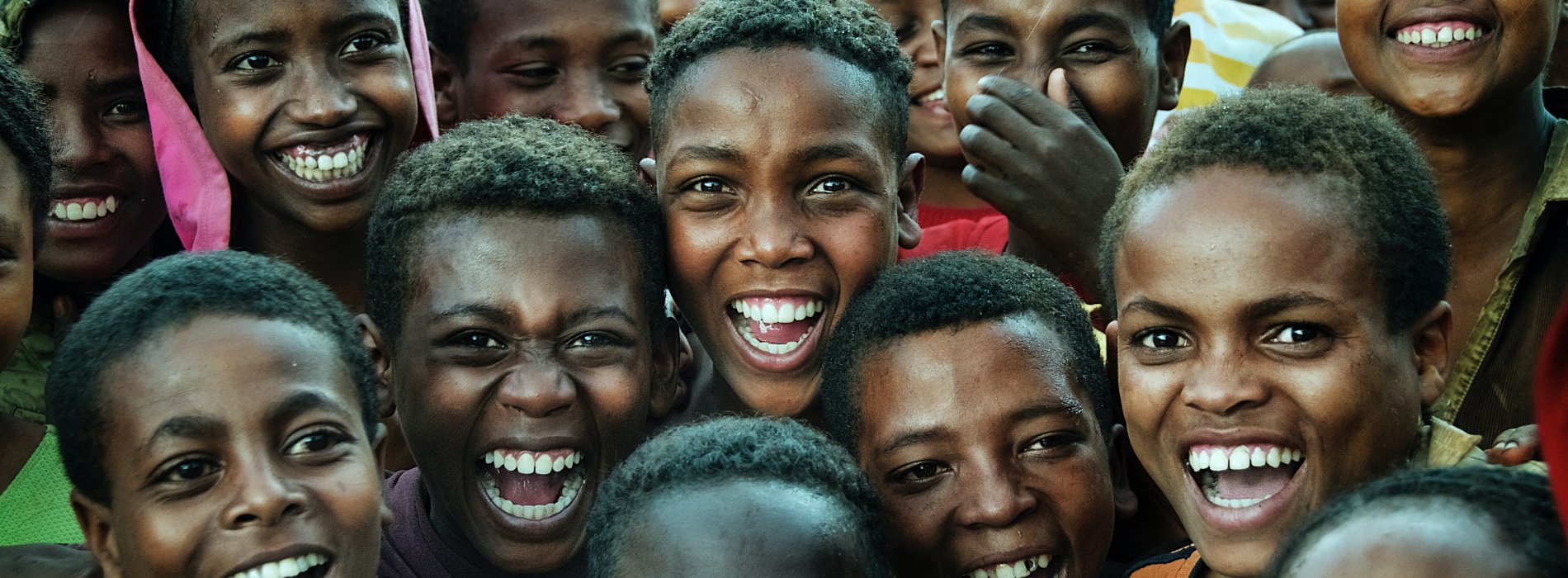 A group of children gathered together joyfully smile at the camera.