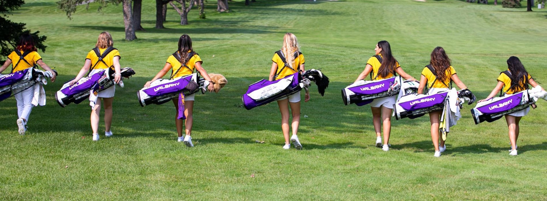 ualbany women's golf team walks up a fairway with their golf bags.