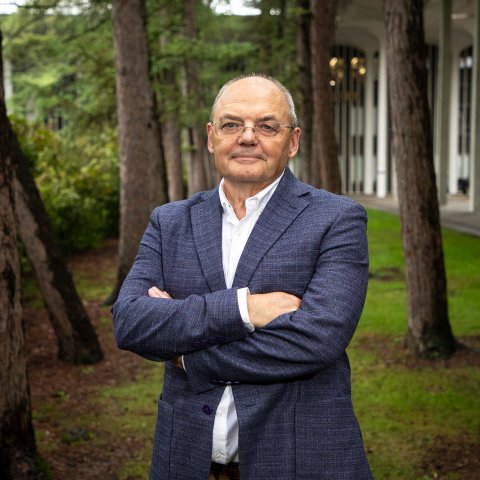 Andrei Lapenas stands in a suit with his arms folded in front of the Academic Podium courtyard on the Uptown Campus.
