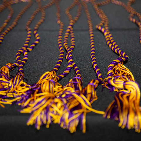 A set of purple and gold stoles lay on a table with a black tablecloth on it.