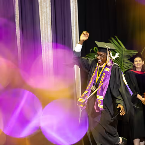 A student celebrates during commencement, a Spellman Award stole draped over their shoulders.