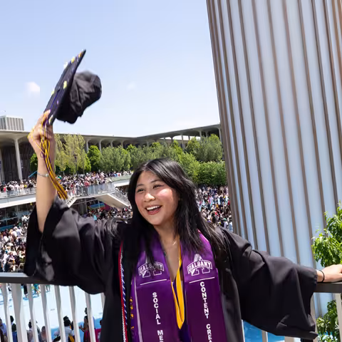 A student celebrates commencement, holding up their cap and smiling.