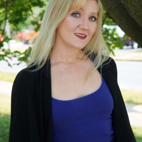 blonde woman in blue shirt and dark sweater under a tree