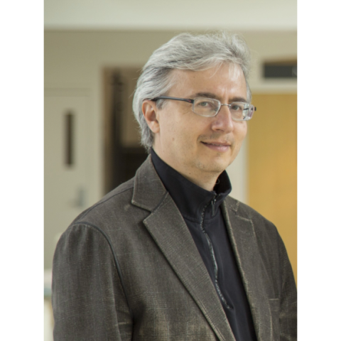 A man with glasses and a brown blazer poses for a portrait
