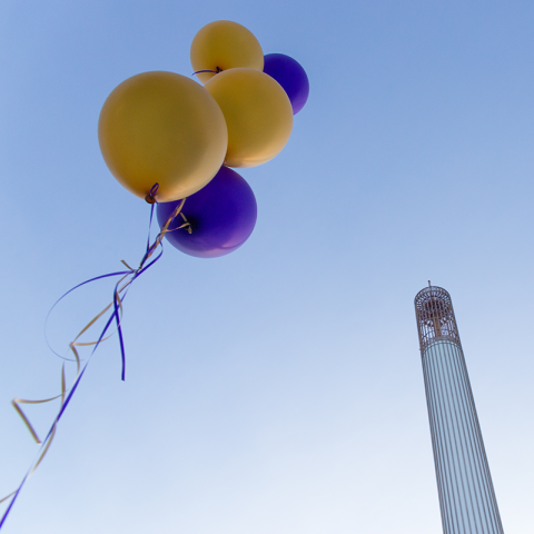 A group of gold and purple balloons float in the sky with the Carillon behind them.