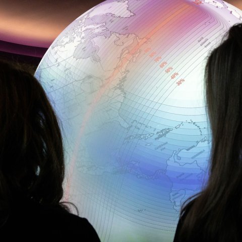 Two people are silhouetted as they look at the bright Science on Sphere globe showing the 2024 solar eclipse's path.