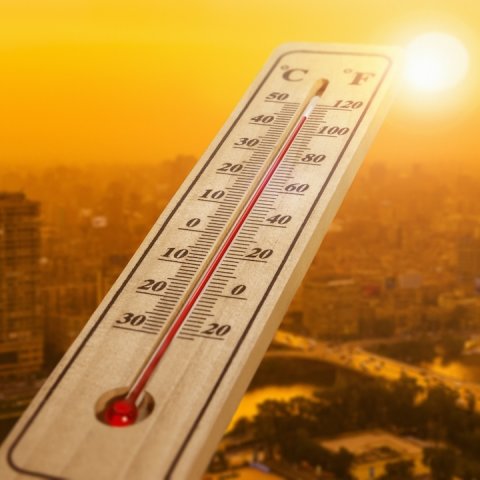Thermometer shown in foreground of sunny, hot desert city vista.