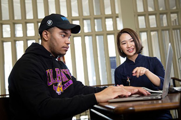 A woman helps a student, who is using a laptop and wearing a UAlbany sweatshirt