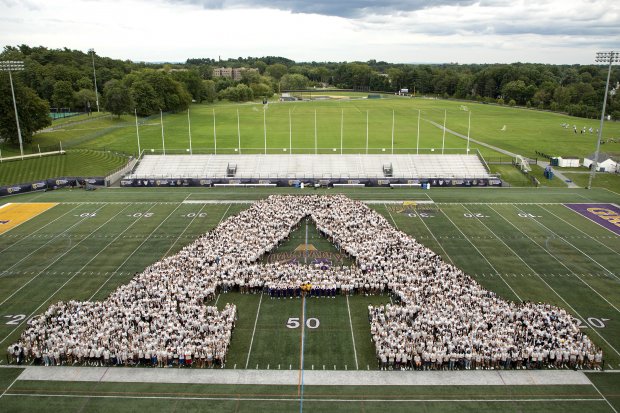 Hundreds of students in matching white t-shirts stand on a turf field in the shape of the UAlbany "A"