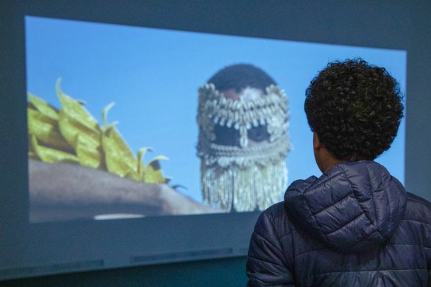 Visitor looking at a projection of a veiled costumed face