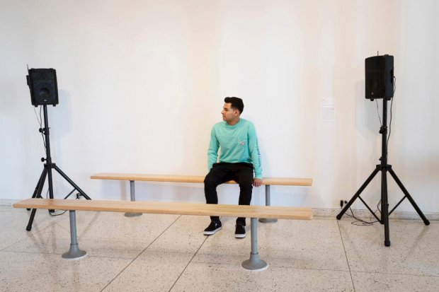 A student sitting on a bench in-between two speakers on stands on either side
