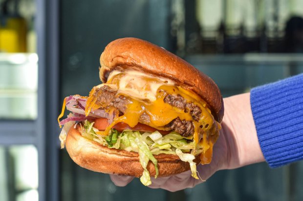 A hand holds out a double cheese burger with lettuce and tomato