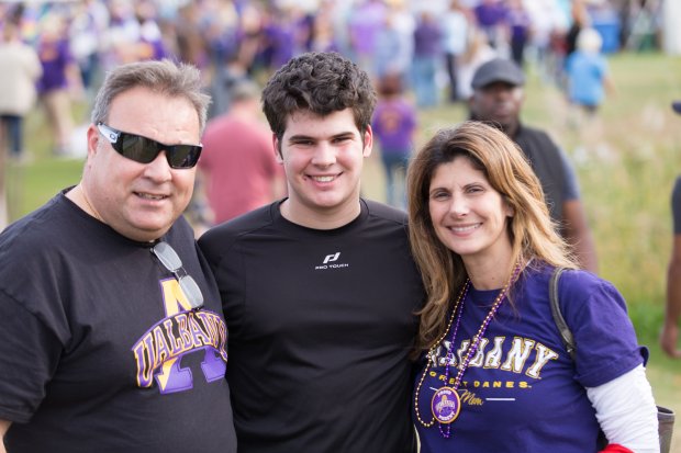 A student posing with his mother and father at a football game. The parents are wearing UAlbany t-shirts.