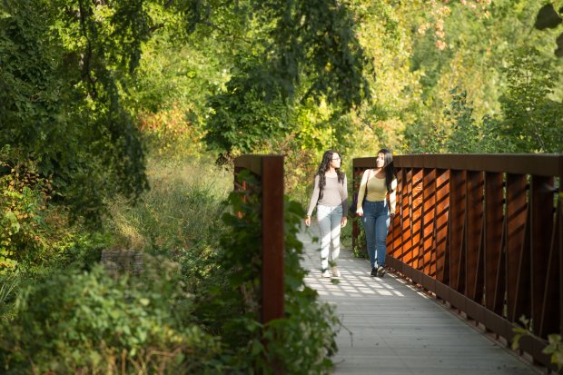 Two people walk across a bridge that spans Indian Pond, a wooded nature area on UAlbany's Uptown Campus