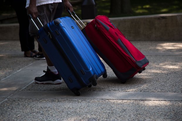 A student walks along a sidewalk with two rolling suitcases