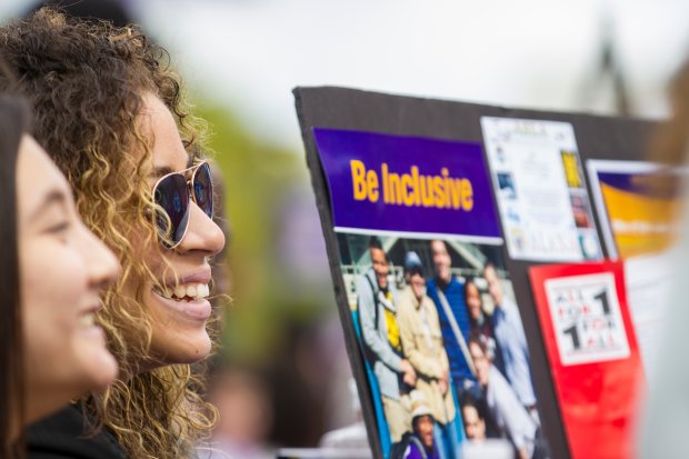 Two students table during the Student Affairs Block Party, smiling beside a poster that says "Be Inclusive"