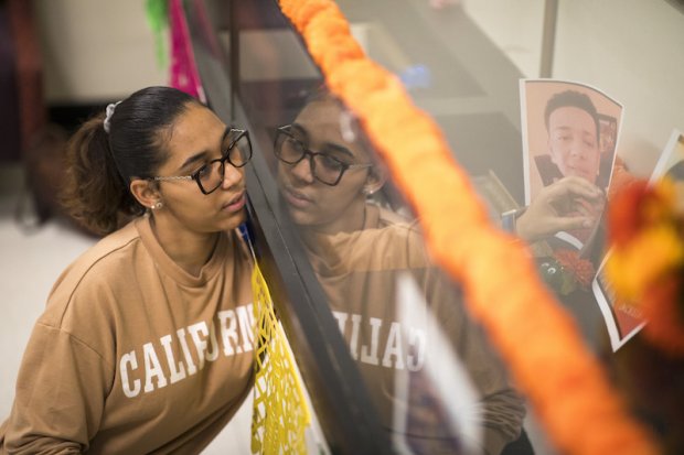 A young woman in glasses places a picture of a lost loved one inside a glass display case that reflects her image back to her.