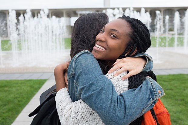 Two students embrace near a fountain, as one of the students smiles into the camera