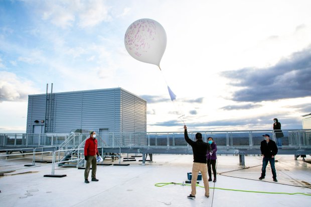 Five researchers stand on a building roof as they release a white weather balloon into the air.