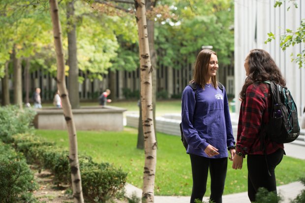 Two students stand outside a residential quad talking and smiling on a spring day