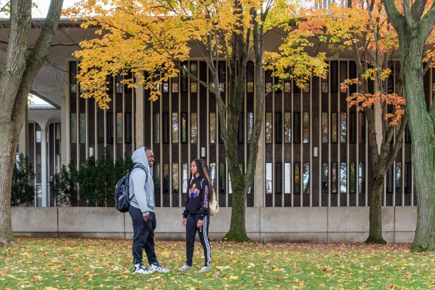 Two students stand outside a residential quad talking and smiling on a fall day