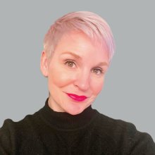 Smiling woman with short pink hair and bright pink lipstick, wearing a green mock turtleneck sweater.