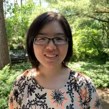 woman with glasses smiling outdoors with trees backdrop