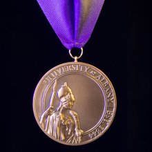 A bronze medallion with the Greek goddess of knowledge, Minerva, and the words, "University at Albany, Est. 1844."