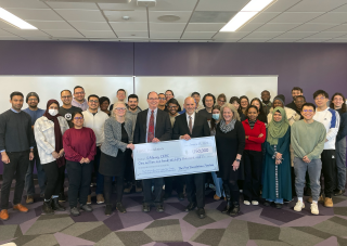 A class of Information Science PhD students stand around a ceremonial $1.15 million check from the First Foundation.