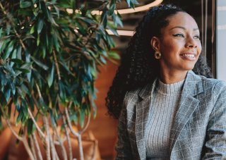 A smiling professional in communications or marketing sitting by a window holding a laptop.