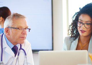 A clinical informatics specialist discusses an EHR-related issue with a doctor.