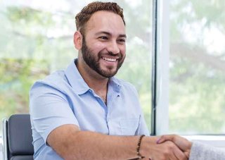A career counselor seated at a desk shakes hands with a client.