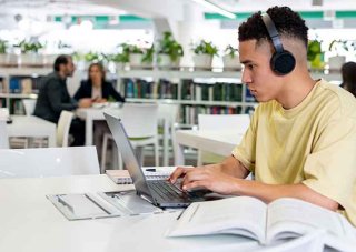 A student on his laptop in the library attends online classes.