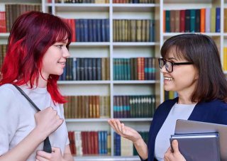 An academic advisor talks to a student in the school library.
