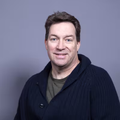 Dr. Backenson smiles at the camera against a grey background.