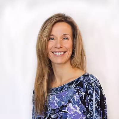 Dr. Stephanie Affinito smiling with white background and blue, purple & black top