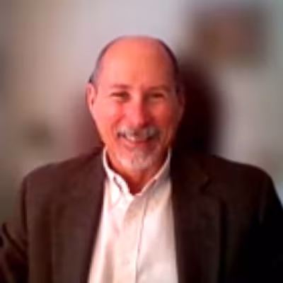 Dr. Michael V. Ellis smiling in white dress shirt and brown jacket with blurred background