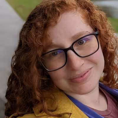 Catarina Alves smiling outdoors with red hair, glasses and yellow jacket