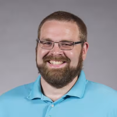 individual in light blue shirt smiling with gray portrait background