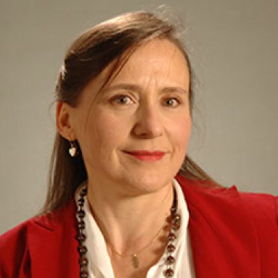 Karin Reinhold wears a red blazer, a red beaded necklace, a silver chain and silver earrings, against a neutral background.