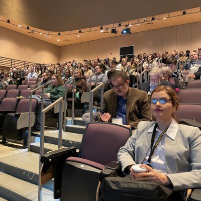 A crowd of people sit in an auditorium looking attentively ahead at the 2023 RNA Institute Annual Symposium