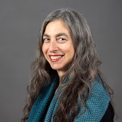 Aviva Bower smiles wearing a black shirt and deep teal scarf against a gray backdrop