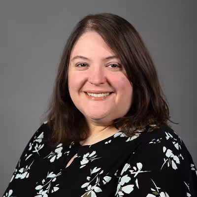 Johanna Cole smiles wearing a black and white floral shirt against a gray backdrop